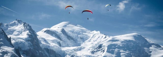 Mont Blanc rising above the Alps with paragliders gliding across the sky.